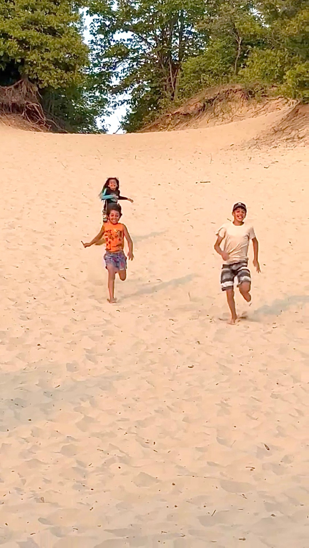 Children running freely down sunlit sand dunes