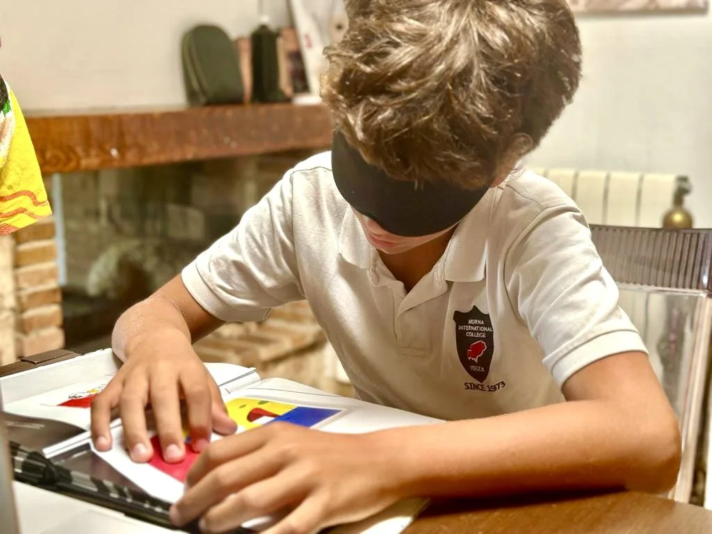 A blindfolded child working independently with hands on a printed page, exploring extraocular perception