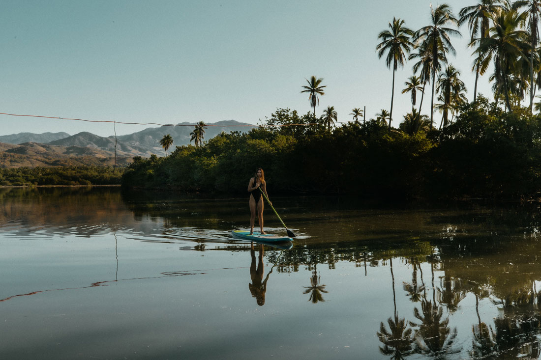 Paddleboarding across a still lagoon framed by palms and mountains at MUSA